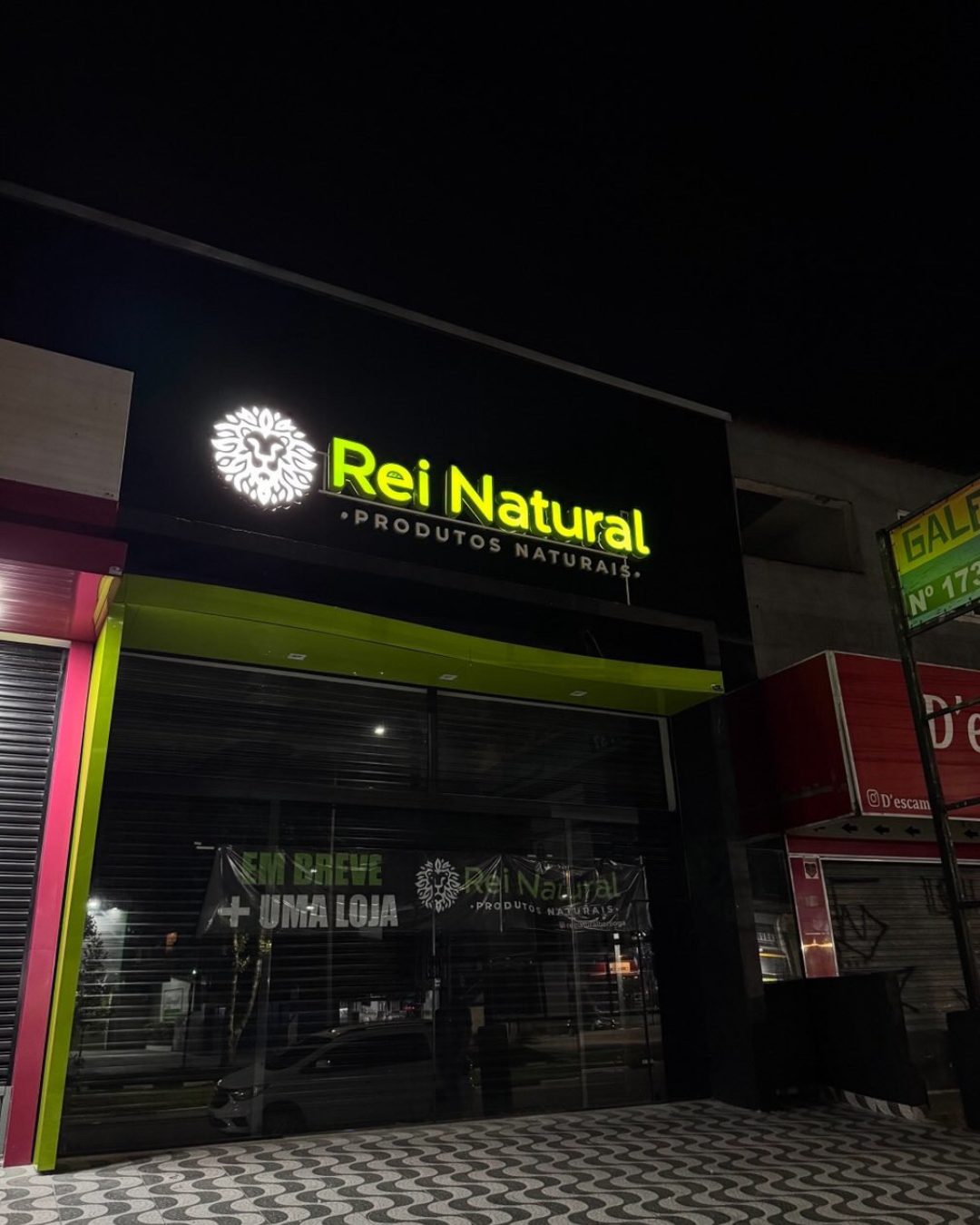 Fachada comercial preta e verde com letreiro iluminado